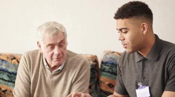 Young care worker sitting with elderly male client
