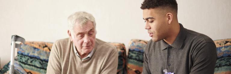 Young care worker sitting with elderly male client